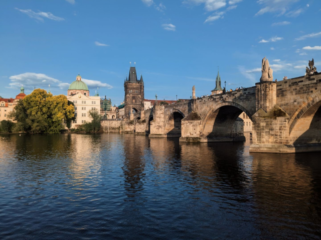 A picture of a medieval stone bridge with a bridge tower in Gothic style. Sunny weather, blue sky.