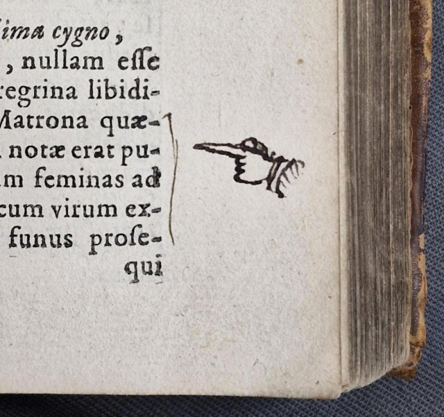A closeup of text in an early printed book with a pointing hand drawn in the margin to draw attention to a particular passage.
