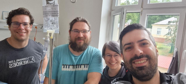 A selfie from the hospital. Tomáš Hnčiar, me, Karolina Surma, Charalampos Stratakis. I have an IV. There's a window behind us.
