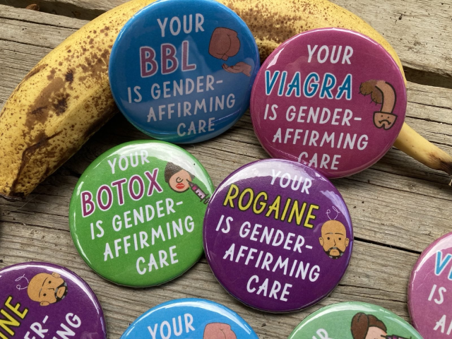 Four circular pin buttons are resting against a banana:
The blue one says "Your BBL is gender affirming care", with a cartoon of a butt and a hand underneath it in a lifting motion.
The pink one says "Your Viagara is gender-affirming care", with a cartoon of a limp penis with a sad face.
The green one says "Your Botox is gender affirming care", with a cartoon of a plump face with red lips, big hair and a strange nose being injected by a large needle.
And the purple one says "Your Rogaine is gender affirming care", with a cartoon of a bald man with two curly wisps of white hair sticking out of his head.