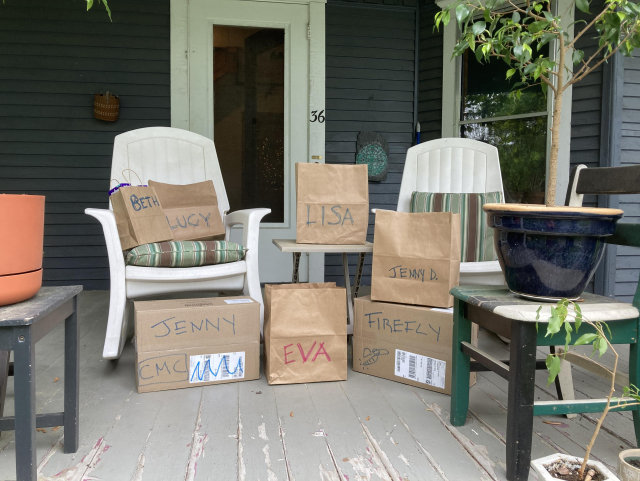 My front porch with five bags and two larger boxes which all have people's names written on them in big block letters. The bags contain COVID tests.