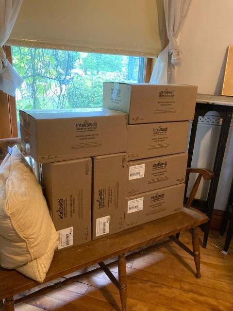 a bench inside my house with seven large boxes full of COVID tests. They say "intelliswab" on the side of them and are stacked tightly but still take up a lot of room.
