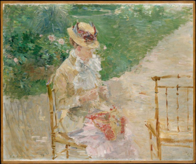 Woman sitting in a chair outside knitting. There are flowers behind her and an empty chair beside her.