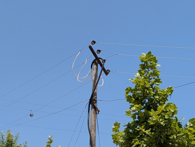Detail of a wooden pole. A black cable loosely attached to the pole is directly tapped to the high voltage line.