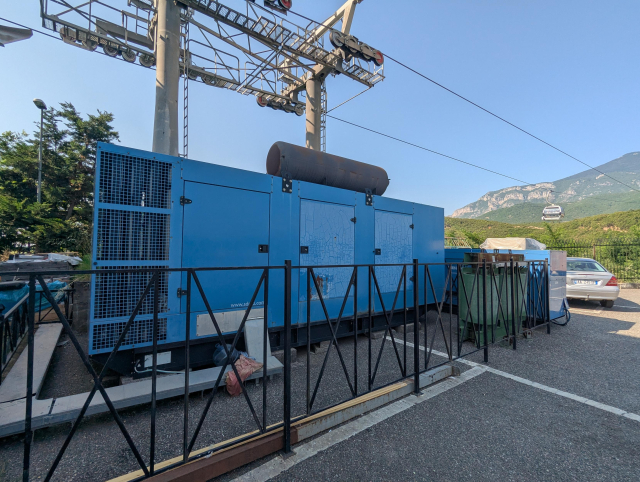 A huge diesel generator underneath the supporting poles of a cable car.