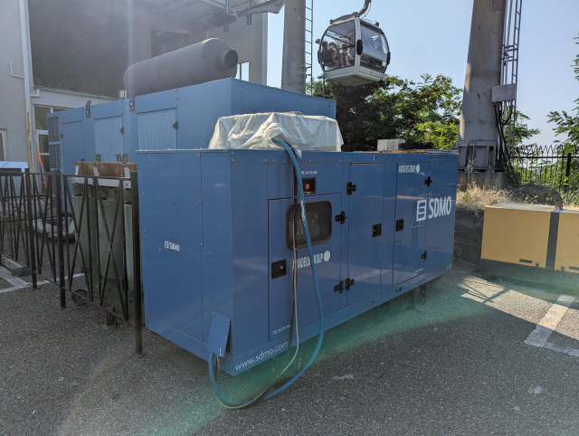 A smaller diesel generator situated next to a bigger one. A gondola of the cable car hangs above.