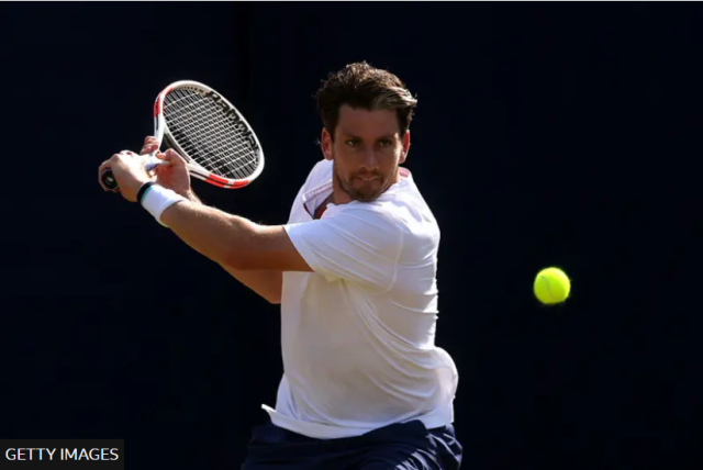 Cameron Norrie is captured mid-action on the court. He is wearing a white shirt and appears focused, preparing to hit a bright yellow tennis ball with his racket using a backhand stroke. 
There is a "Getty Images" watermark in the corner.