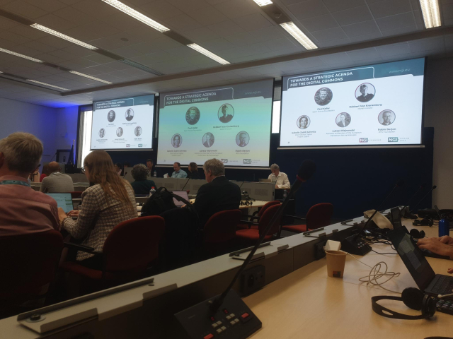 Photo of conference room with panel speakers and audience members shown from the back.