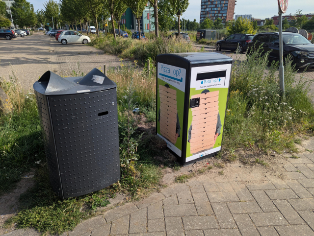 A trashcan for pizza boxes next to a regular trashcan. The pizza box trashcan carries the logo of the municipality of Zaanstad.