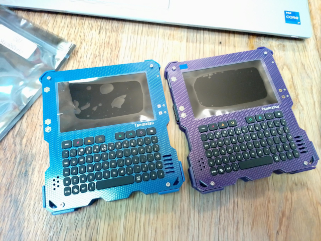 Two squarish, cyberdeck like devices with a screen and a keyboard. One is blue, the other purple