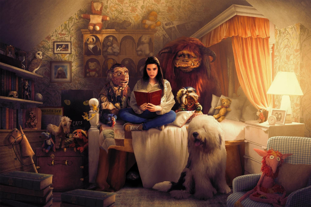 Illustration showing Sarah from the Labyrinth sitting in her bedroom, wearing her distinctive outfit from the film, sitting with her legs crossed on the bed holding a book and reading it with visible fascination as she is surrounded by most of the main characters from the film including Hoggle the dwarf, Ludo, a brown horned beast, William the worm, a blue worm-like creature wearing a tiny red scarf around its neck, Sir Didymus a talking Yorkshire Terrier wearing an eye patch and Ambrosius the dog sitting next to the bed near them. In the room there are several items referencing both the film and other Jim Henson works including the Muppets and The Dark Crystal, including a picture of Henson himself holding Kermit the frog hanging on the wall.