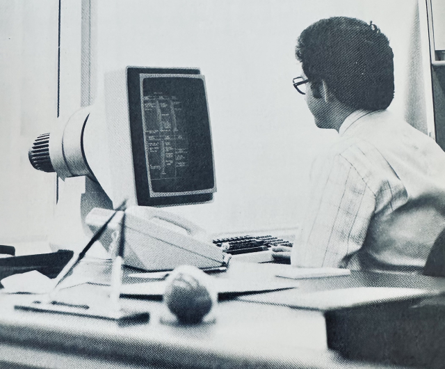 Photo of a worker at a bank working on a monochrome monitor that looks a bit like a jet engine, ca. 1981