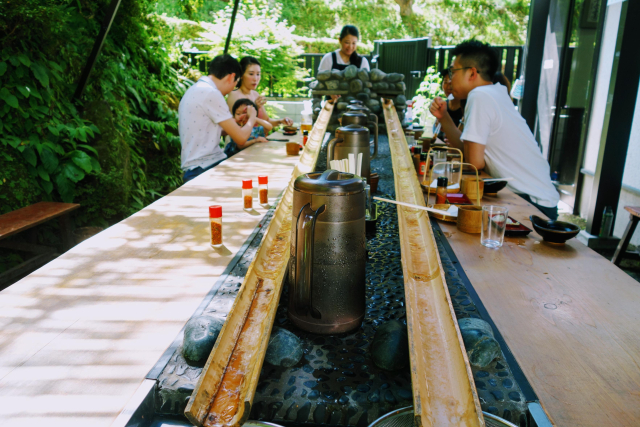 Zoom out we see people sitting at benches/tables in front of the noodle slides 
