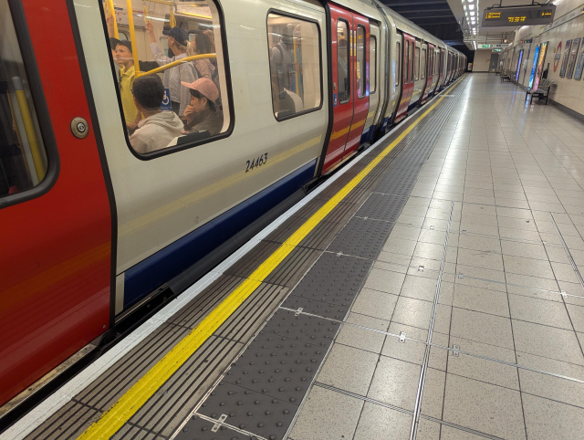A view of a train of London Underground standing by a platform with doors closed. There's a tiny gap between the train and the platform.