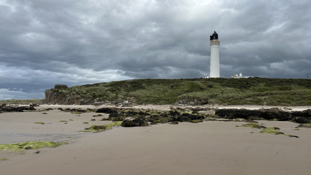 Lighthouse on a cliff above a beach at low tide. 