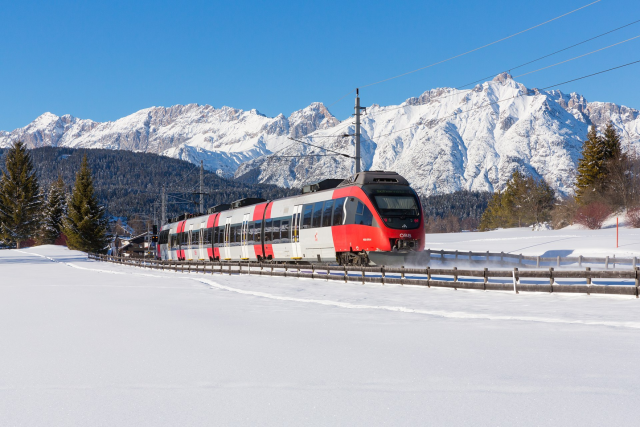 a Bombardier Talent train in ÖBB livery approaching Seefeld in Austria, with the tracks covered in snow and the Alps in the background