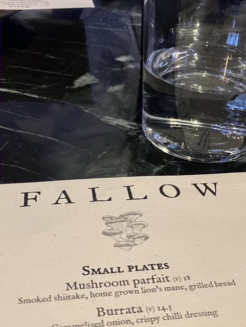 The top part of the menu of Fallow, a restaurant in London, and a glass of water on a dark table