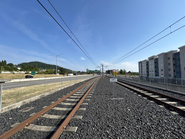 Looking toward the end of the green line tracks in Clackamas. Highway is to the left. Some mid-rise buildings to the right.