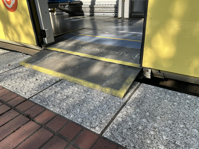 A close-up view of the interface between a yellow MAX light rail train and a platform, where a short ramp has extended from the bottom of the train door down to the platform, only a several-centimeter gap horizontally and vertically.