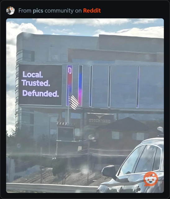 View of the WGBH building in Boston with an electronic marquee reading “Local. Trusted. Defunded.”