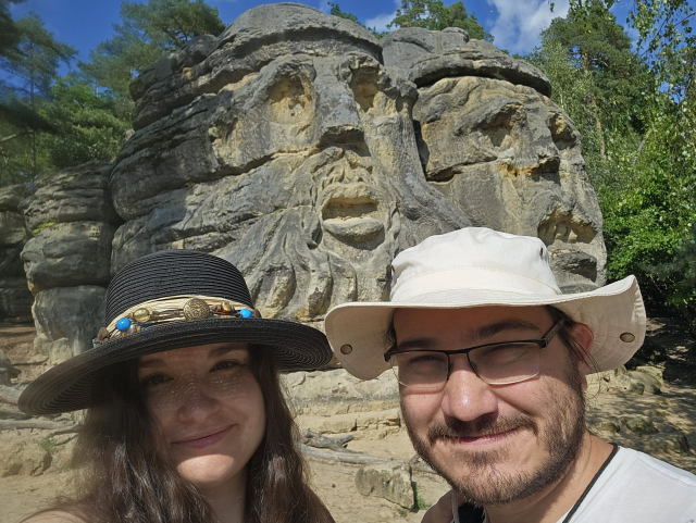 Selfie of me and Anna in front of  a sandstone rock with two huge head reliefs sculpted in it.