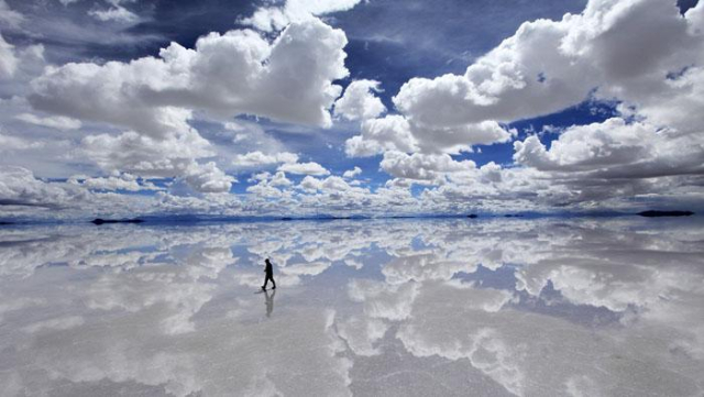 A single person traverses the mirror of a deep blue sky filled with cotton wool clouds