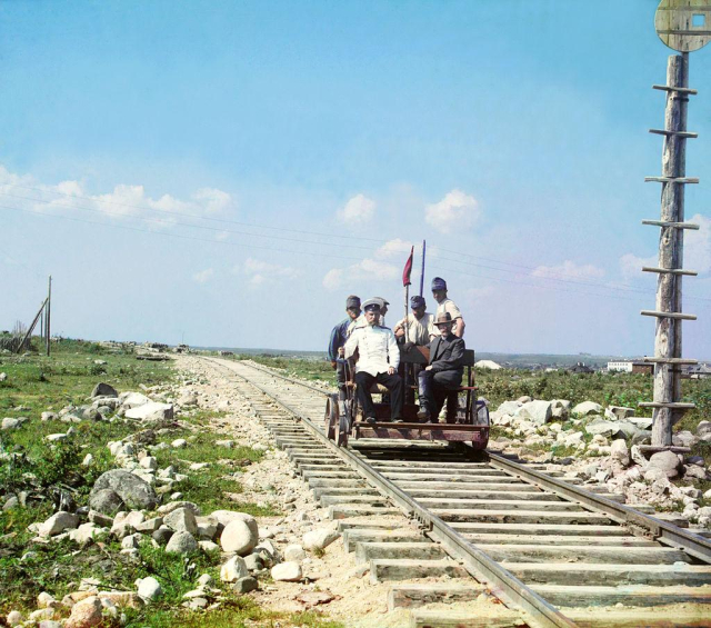 Mr. Prokudin-Gorsky himself sat in a rail handcar with four other men on the Murmansk railroad. the other men are wearing some kind of uniform, while Mr. Prokudin-Gorsky wears a suit. the sky is blue and the weather looks fair.
