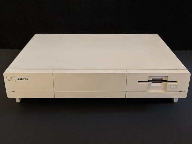 the computer alone with no monitor. it's about the size of a pizza box but it is twice as thick. there's a rainbow checkmark logo in the left corner next to the "Amiga" text logo.