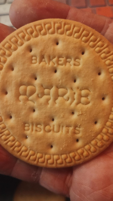 One of the Marie biscuits being held in a hand, the name stamped onto the face of the biscuit