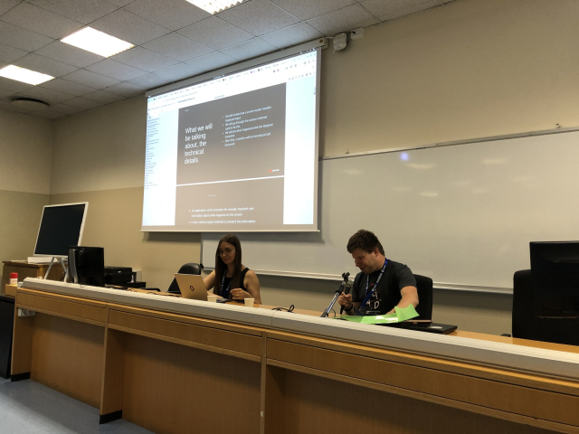 Lukáš at the microphone, presentation being projected behind him, and Vera changing slides at the laptop.