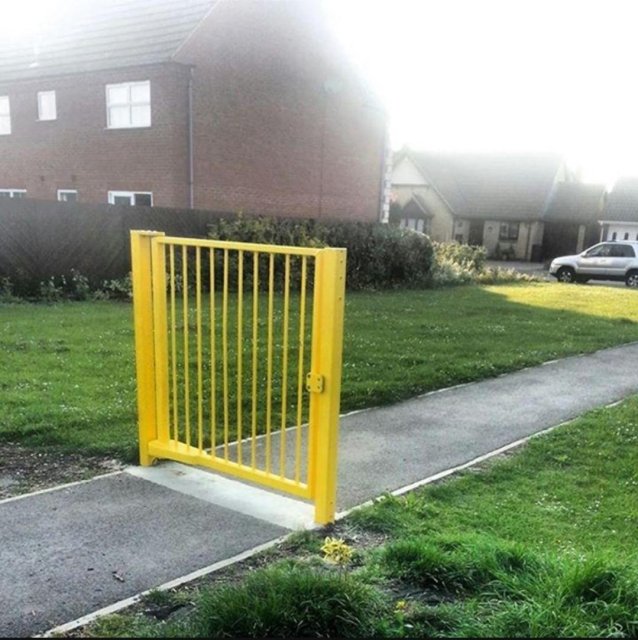A yellow gate on a concrete path. There is no fence to either side making it trivial to bypass