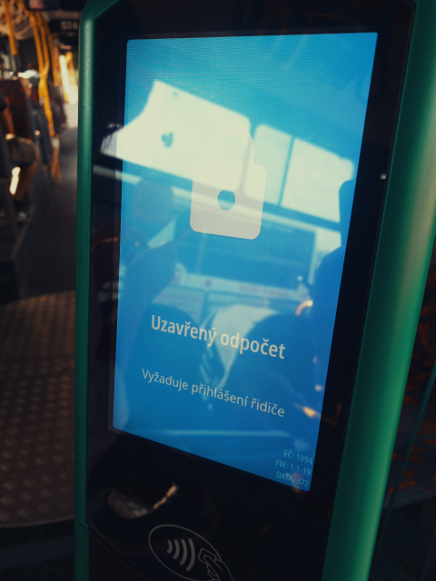 Uvnitř autobusu se nachází zeleně orámovaný terminál pro odbavení cestujících s velkým modrým dotykovým displejem. Na obrazovce svítí bílá ikona zamčeného zámku a text „Uzavřený odpočet – Vyžaduje přihlášení řidiče“.