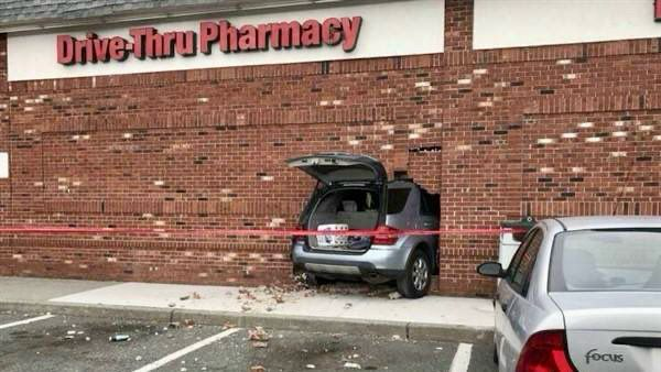 A silver SUV has crashed into the side of a brick building marked "Drive-Thru Pharmacy."