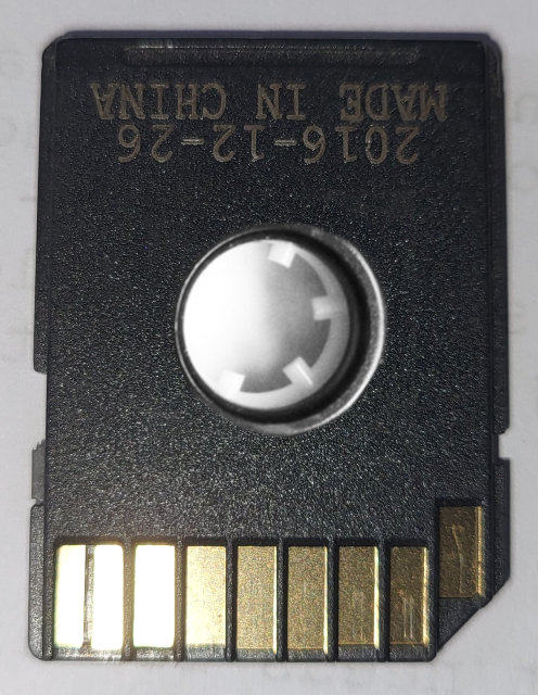 SD Card with a tape cassette spool wheel in the centre, and copper contacts to to bottom.