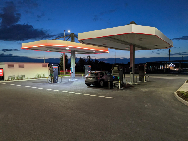 A charging station with one car being charged. The sky in the background is dark, around sunset.