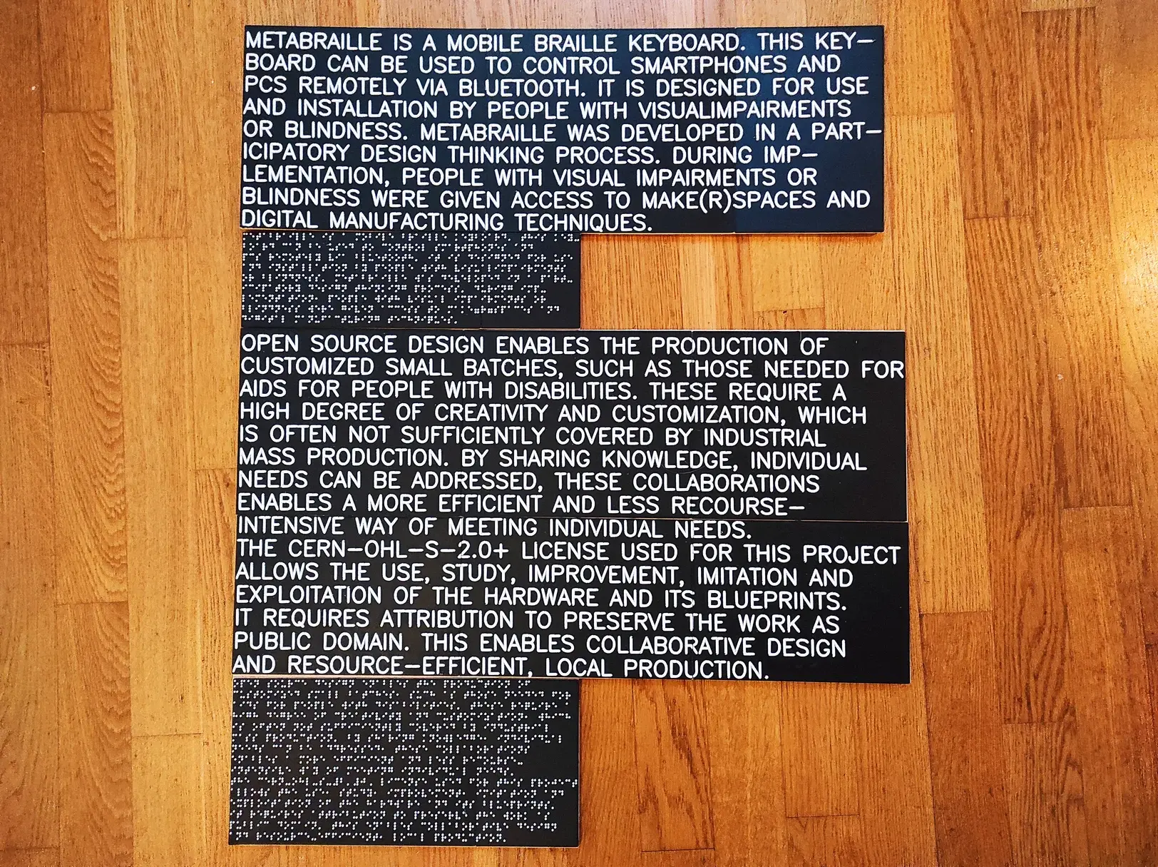 3D printed descriptions for an exhibition. The lettering is white on a black background. The text is presented in Braille and tactile print. The signs lie on a parquet floor

Description of Metabraille  
Metabraille is a mobile Braille keyboard. This keyboard can be used to control smartphones and PCs remotely via Bluetooth. It is designed for use and installation by people with visual impairments or blindness. Metabraille was developed in a participatory design thinking process. During implementation, people with visual impairments or blindness were given access to Make(r)spaces and digital manufacturing techniques.

Description of open source hardware  
Open source design enables the production of customized small batches, such as those needed for aids for people with disabilities. These require a high degree of creativity and customization, which is often not sufficiently covered by industrial mass production. By sharing knowledge, individual needs can be addressed, these collaborations enable a more efficient and less recourse-intensive way of meeting individual needs. The CERN-OHL-S-2.0+ license used for this project allows the use, study, improvement, imitation and exploitation of the hardware and its blueprints. It requires attribution to preserve the work as public domain. This enables collaborative design and resource-efficient, local production.
