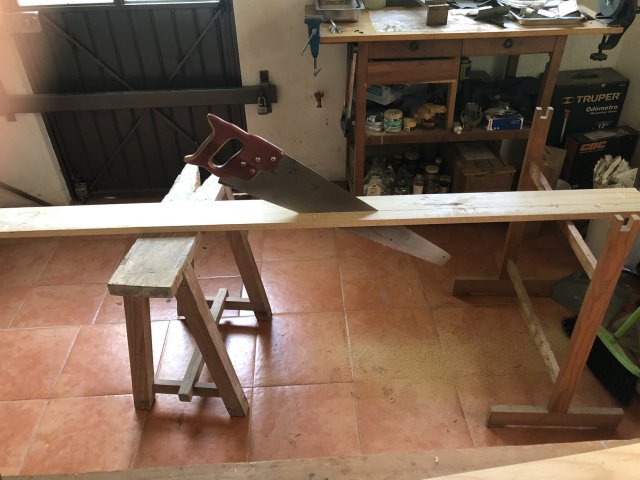 El serrucho de corte longitudinal, a la mitad del corte de una tira larga de madera. La tabla está puesta sobre dos burritos para serruchar.