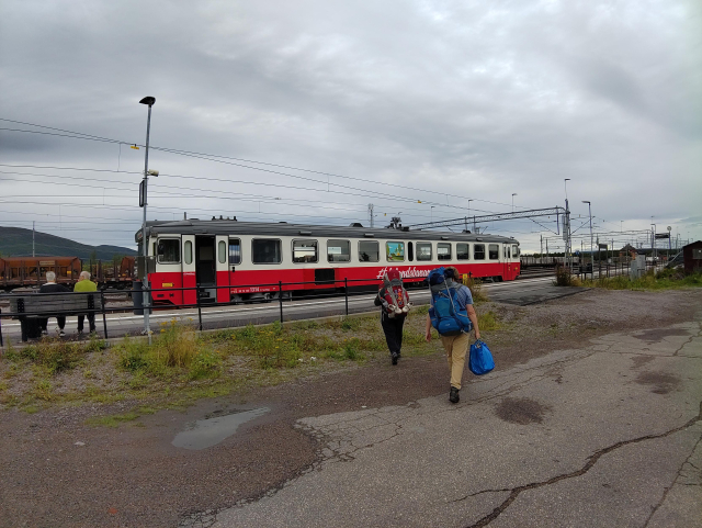 Die Inalndsbanan steht in Gällivare auf dem Bahnhof. Davor sind Menschen mit großen Rucksäcken zu sehen.