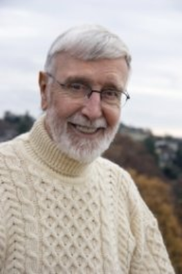 Dave Duncan:  an older man with white hair and a beard, smiling toward the camera, wearing glasses. Dressed in a cream-colored, cable-knit turtleneck sweater in an outdoor setting