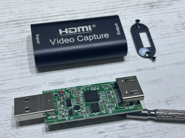 Teardown of a basic HDMI capture card. At the top, the metal empty hosing. And at the bottom, the printed circuit board with a USB type A connector on the left, and an HDMI port in the right. There is one main chip, and many supporting components. 