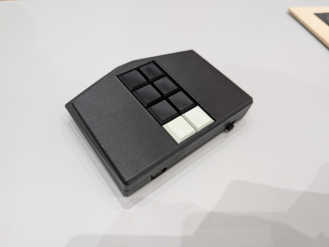 Ein flaches, fünfeckiges Gerät aus dem 3D-Drucker mit 10 Tasten auf der Oberseite liegt auf einem Tisch.