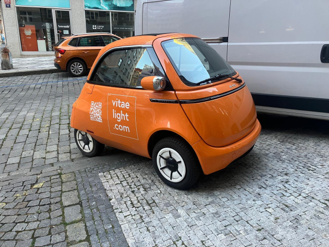 Orange Microlino electric bubble car on cobbled Prague street