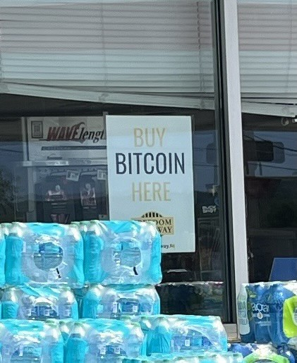 A zoom in of the prior photo. It shows a white card a little bigger than a letter sized sheet of paper with big letters saying buy bitcoin here. 