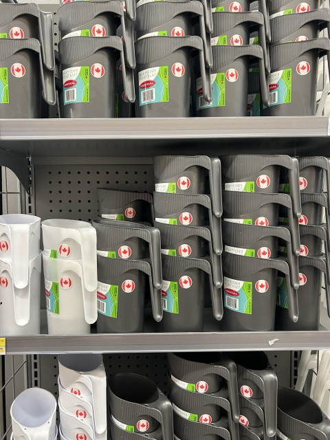 A shelf with a bunch of plastic pitchers labeled with a “Made in Canada” sticker. They are white or gray.
