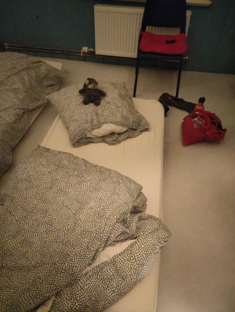 A mattress with duvet and pillow on the floor with Frida (the sleepy teddy bear) sitting on the pillow. A rope bag lies next to it.