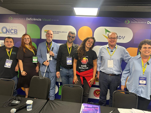 Photo of presenters and moderators for the session:  "Digital Access for All – Creating Inclusive Information Spaces".  From left to right, Octavio Carreno and Mariana Pinheiro, Marc Workman, Flavio Correia, Simone Freire, James Boreham, and Emma Bennison. All are standing side by side, smiling, in front of the World Blindness Summit backdrop in São Paulo.