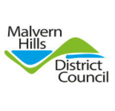 logo of Malvern Hills District Council. It features the text "Malvern Hills District Council" in black letters. The words "Malvern Hills" are aligned to the left, and beneath them are the words "District Council," also aligned to the left. Between the two sets of words is a stylized design of two overlapping, curved shapes. The top shape is green, resembling a hill, while the lower shape is blue, suggesting a valley or body of water. These shapes are intertwined, reflecting a sense of landscape. The overall design integrates the text with the graphic elements to represent the district's geographic features.