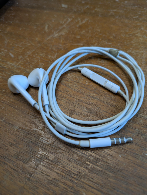 a looped up set of vintage OEM wired ear buds in Apple white except for being dingy with years of use