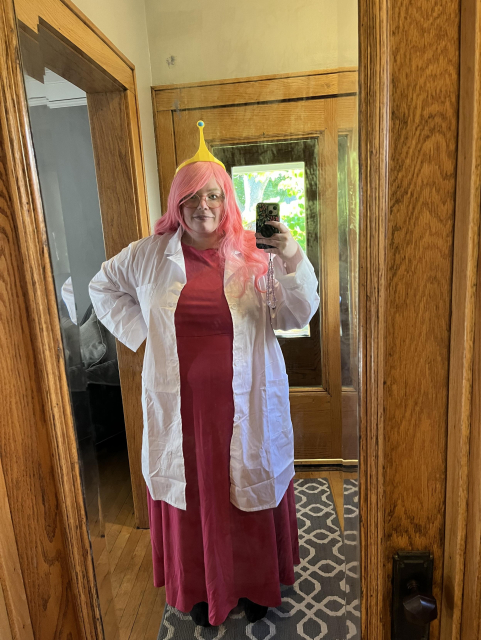 Ashe dressed up as Princess Bubblegum from Adventure Time. She is wearing a pink dress, a lab coat, a long pink wig, and a yellow crown.