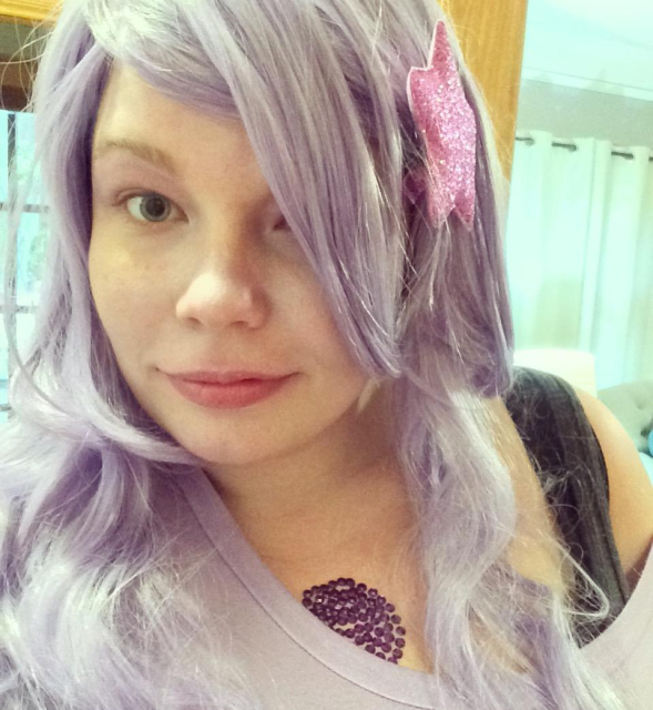 Ashe dressed as Amethyst from Steven Universe. She has a long light purple wig with a pink glittery star hair clip, a light purple shirt, and a circle of purple rhinestones on her chest.